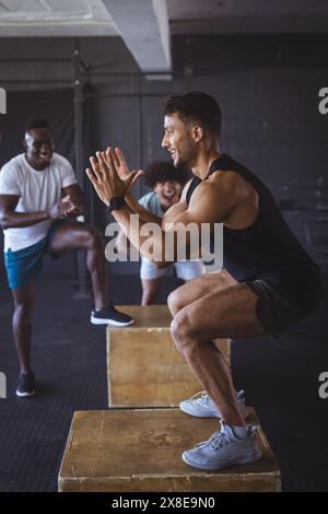 Eine Gruppe verschiedener Männer im Fitnessstudio trainiert zusammen und führt Boxsprünge aus. Sie befinden sich in einem geräumigen, gut ausgestatteten Fitnessraum mit Schwerpunkt auf Kraft und Enduran Stockfoto