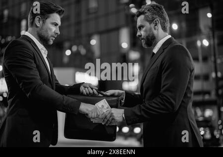 Ein Geschäftsmann, der seinem Partner Geld gibt, während er einen Vertrag schließt. Ein Geschäftsmann, der draußen Geld spendet. Sie zählen uns Dollarscheine, Geld, Finanzmitarbeiter Stockfoto