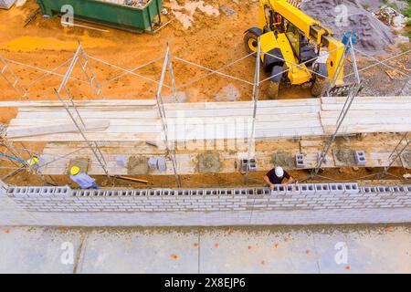 Maurer baut eine funktionierende Betonwand aus Betonblöcken, während er auf Gerüsten steht Stockfoto
