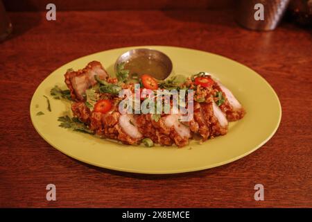 Knuspriger Schweinebauch garniert mit frischen Kräutern, dünn geschnittenen roten Chilischoten und knusprigen Knoblauchstückchen. Stockfoto