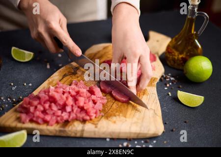 Frau Schnitt Thunfischsteak in Scheiben auf einem hölzernen Schneidebrett in der Hausküche Stockfoto