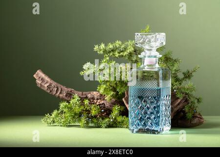 Blauer Gin in Karaffe auf einem Hintergrund von alten Schlingen und wacholderzweigen mit Beeren. Grüner Hintergrund mit Kopierraum. Stockfoto