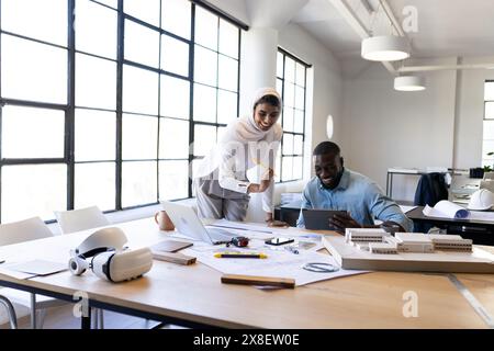 Vielfältiges Team, das an Architekturprojekten in modernen Büros arbeitet. Junger afroamerikanischer männlicher Kollege, der Tablette benutzt, während ein junges indisches weibliches Team führt Stockfoto