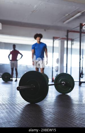 Afroamerikanische und birassische junge Männer im Fitnessstudio, fit und konzentriert sich auf ihr Workout. Umgeben von gut beleuchteten Fitnessgeräten, einschließlich Langhantel auf dem Boden Stockfoto