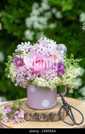 Romantisches Blumenarrangement mit rosafarbener Rose, Bratschenblüte, bellis, kolumbine und beautybusblüten in einer Tasse Stockfoto