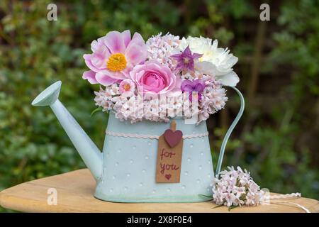 Romantisches Blumenarrangement mit rosafarbenen Pfingstrosenblüten, Bratschenblüten, bellis, kolumbine und Schönheitsbuschblüten in dekorativer Gießkanne Stockfoto