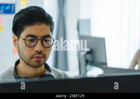 Der Prompt-Ingenieur des asiatischen Mannes entwickelt eine Codierungs-App mit Softwaredaten, die vor dem Computermonitor im Büro sitzen Stockfoto