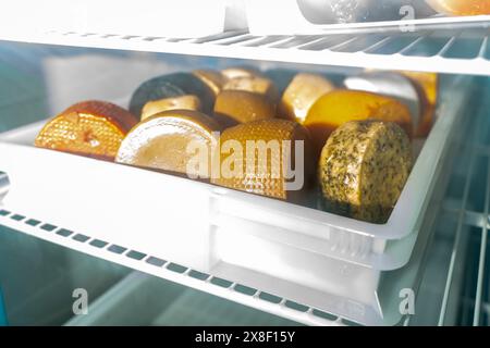 Ein Haufen verschiedener Käsekreise auf dem Regal des Kühlschranks. Käsemädel in der Alterungskammer einer kleinen Käsefabrik. Hoher ph-Wert Stockfoto