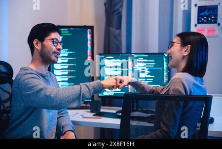 asiatische und indische Entwicklerteams klatschen sich für Projekterfolg mit Software-Computer in der Nacht im Büro Stockfoto