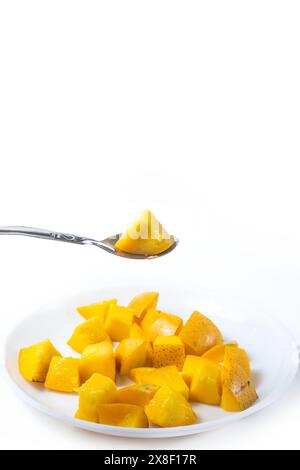 Mangoscheiben auf weißer Platte mit Löffel isoliert auf weißem Hintergrund. Vertikale Aufnahme. Stockfoto