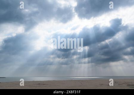 Dramatische Sonnenstrahlen durchdringen die schwere Wolkendecke, um den ruhigen Strand zu beleuchten. Stockfoto