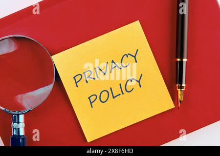 Text der Concept Privacy Policy auf einem gelben Aufkleber auf einem roten Business-Notizbuch in einer Komposition mit Lupe und Füllfederhalter Stockfoto