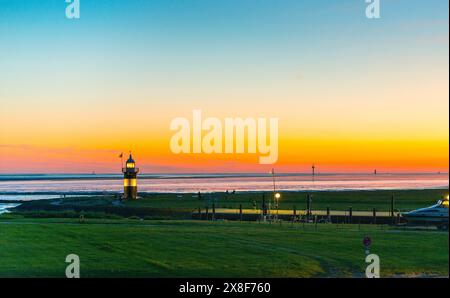 Schwarz-weißer Leuchtturm, „kleine Preusse“ genannt, Leuchtturm und Boot bei Sonnenuntergang an der Küste, Himmel in warmen Farben, orangefarbener Himmel mit Farbe Stockfoto