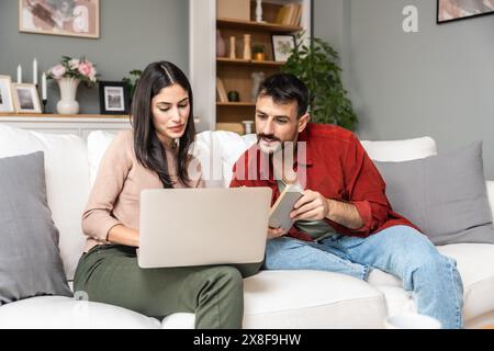 Einfaches Leben. Glückliches junges Paar, Mann und Frau sitzen entspannt auf der Couch im Wohnzimmer, lesen Buch trinken Tee zusammen, surfen im Internet, beruhigen Stockfoto