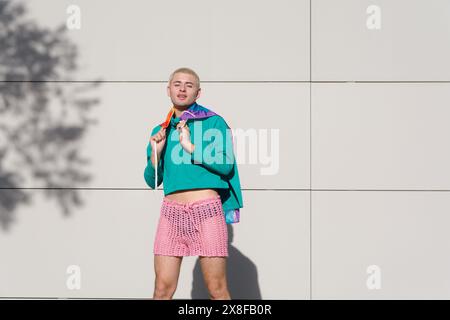 Ein junger Lateinmann in grünem Hemd und rosa Shorts posiert für ein Foto mit einer Stolzfahne auf den Schultern, er steht draußen in der Nachmittagssonne l Stockfoto