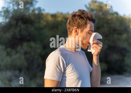 Kranker Mann umgeben von der Natur bläst sich die Nase und niest für Pollenallergiesymptome Stockfoto