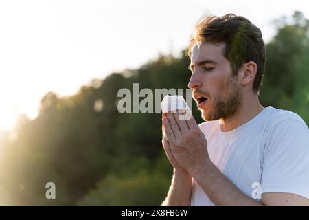 Kranker Mann umgeben von der Natur bläst sich die Nase und niest für Pollenallergiesymptome Stockfoto