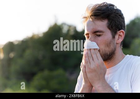 Kranker Mann umgeben von der Natur bläst sich die Nase und niest für Pollenallergiesymptome Stockfoto