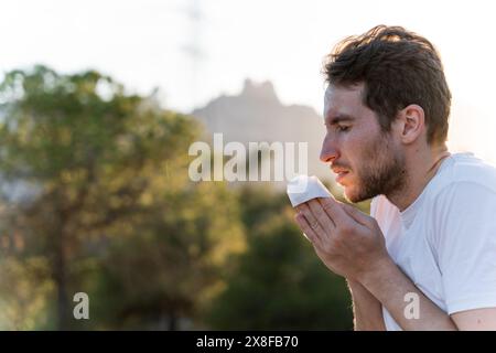 Kranker Mann umgeben von der Natur bläst sich die Nase und niest für Pollenallergiesymptome Stockfoto