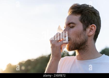 Kranker Mann umgeben von der Natur bläst sich die Nase und niest für Pollenallergiesymptome Stockfoto