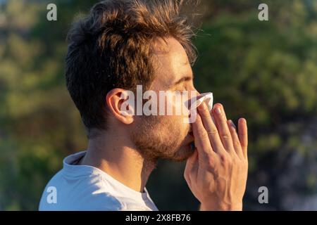 Kranker Mann umgeben von der Natur bläst sich die Nase und niest für Pollenallergiesymptome Stockfoto