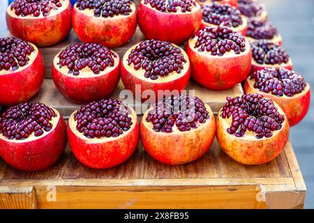 Granatapfel mit der Oberseite abschneiden die Früchte und saftigen Samen an einem Marktstand. Zubereitung von Granatapfelsaft. Stockfoto