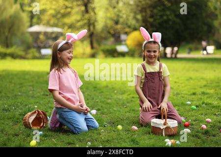 Osterfeier. Süße kleine Mädchen in Hasenohren jagen Eier draußen Stockfoto