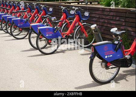 Viladecans, Barcelona, Spanien-25. Mai 2024: Reihe von roten und blauen öffentlichen Fahrrädern, Teil eines Bike-Sharing-Programms, parkt ordentlich vor einem Holzzaun W Stockfoto