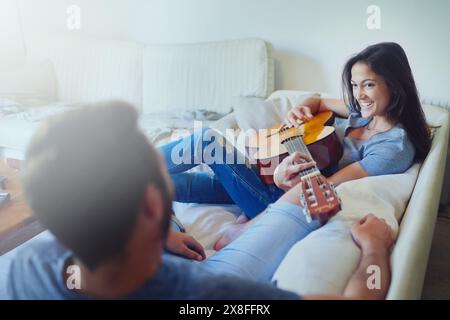 Paaren Sie, Gitarre und entspannen Sie sich auf dem Sofa mit Musik am Morgen mit Sorgfalt, Verbundenheit und Kreativität im Wohnzimmer zu Hause. Mann, Frau und Künstler mit einem Lächeln, denken Stockfoto