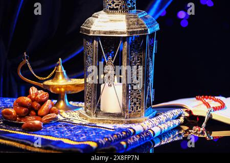 Arabische Laterne, Koran, misbaha, Aladdin Zauberlampe, Datteln und gefaltete Gebetsmatte auf Spiegeloberfläche bei Nacht Stockfoto