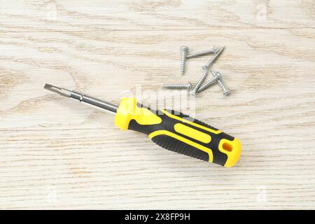 Schraubendreher mit gelbem Griff und Schrauben auf weißem Holztisch, flach gelegt Stockfoto