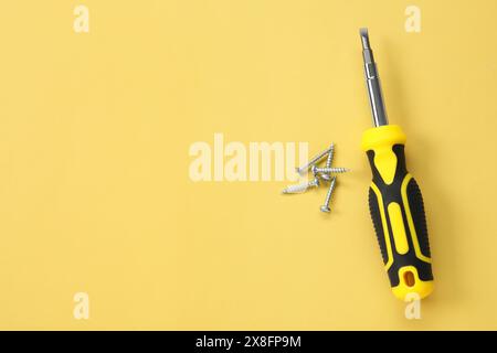 Schraubendreher mit schwarzem Griff und Schrauben auf hellgelbem Hintergrund, flach gelegt. Leerzeichen für Text Stockfoto