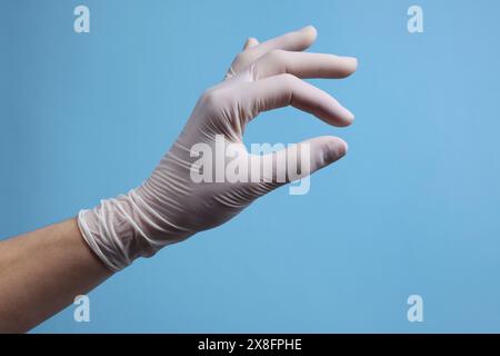 Doktor trägt weißen medizinischen Handschuh, der etwas auf hellblauem Hintergrund hält, Nahaufnahme Stockfoto