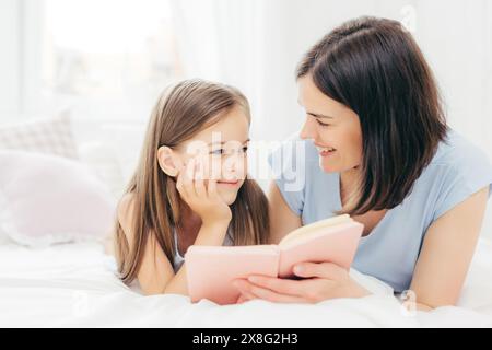In gemütlicher Geschichte teilen sich Mutter und Tochter einen märchenhaften Moment in einem sonnendurchfluteten Schlafzimmer. Stockfoto