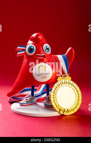 ZHONGSHAN China-23. Mai 2024: Das Maskottchen der Olympischen Spiele 2024 in Paris mit Goldmedaille auf rotem Hintergrund in vertikaler Komposition. Stockfoto