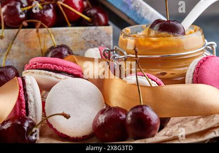 Ein wunderschöner weißer Teller mit bunten Makronen und frischen Kirschen auf einem Tisch, der eine wunderbare Kombination aus Backwaren und zeigt Stockfoto