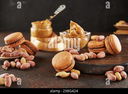 Ein Glas Erdnussbutter, ein Grundnahrungsmittel, wird neben Macarons und Erdnüssen auf den Tisch gestellt. Diese Zutaten können in verschiedenen Kochrezepten verwendet werden Stockfoto