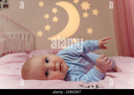 Das Baby liegt friedlich auf einem Bett mit einem Himmelsmotiv mit Mond und Sternen, was eine ruhige und bezaubernde Atmosphäre schafft. Stockfoto