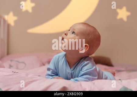 Das Baby liegt friedlich auf einem Bett mit einem Himmelsmotiv mit Mond und Sternen, was eine ruhige und bezaubernde Atmosphäre schafft. Stockfoto