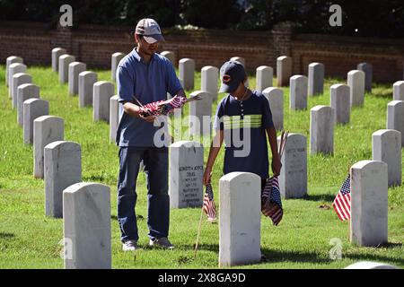 Raleigh, NC, USA, 25. Mai 2024; ein Vater und ein Sohn schließen sich freiwilligen Helfern an, die vor dem Memorial Day die 6.000 Grabsteine auf dem Raleigh National Cemetery mit Fahnen versehen. Die jährliche Veranstaltung, die von der Raleigh American Legion organisiert wird, ehrt die amerikanischen Männer und Frauen, die in Friedenszeiten und Krieg im US-Militär gedient haben. Der Raleigh National Cemetery umfasst die Grabstätten von Soldaten aus dem Bürgerkrieg bis zu den Kriegen im Irak und Afghanistan. Credit D Guest Smith / Alamy Live News Stockfoto