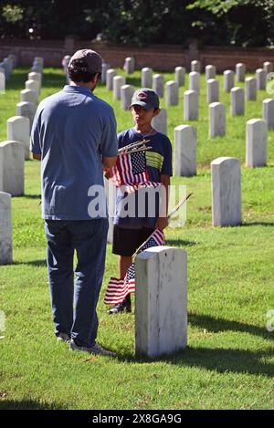 Raleigh, NC, USA, 25. Mai 2024; ein Vater und ein Sohn schließen sich freiwilligen Helfern an, die vor dem Memorial Day die 6.000 Grabsteine auf dem Raleigh National Cemetery mit Fahnen versehen. Die jährliche Veranstaltung, die von der Raleigh American Legion organisiert wird, ehrt die amerikanischen Männer und Frauen, die in Friedenszeiten und Krieg im US-Militär gedient haben. Der Raleigh National Cemetery umfasst die Grabstätten von Soldaten aus dem Bürgerkrieg bis zu den Kriegen im Irak und Afghanistan. Credit D Guest Smith / Alamy Live News Stockfoto