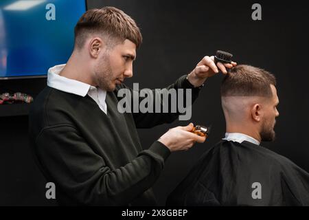 Der junge Friseur trimmt im Friseurladen fachmännisch die Haare eines Mannes mit einem Trimmer Stockfoto