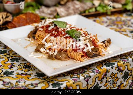 Nahaufnahme eines Tafelgerichts mit „Spaghetti alla Norma“ – Tomatensauce, Auberginen und frischem Basilikum, garniert mit geriebener Ricotta-Salate – klassischer italienischer Pas Stockfoto