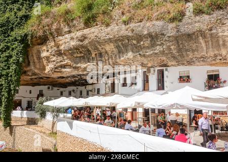 Restaurants und Cafés drängen sich unter einem Felsüberhang entlang der Terrazas Calle Cuevas del Sol in den einzigartigen Pueblos blanco von Setenil de las Bodegas, Spanien. Die Bewohner des kleinen Dorfes Setenil leben seit dem neolithikum in Höhlenhäusern. Stockfoto