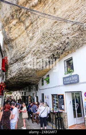 Restaurants und Cafés drängen sich entlang der Calle Cuevas de la Sombra unter dem Felsvorsprung in den einzigartigen Pueblos blanco von Setenil de las Bodegas, Spanien. Die Bewohner des kleinen Dorfes Setenil leben seit dem neolithikum in Höhlenhäusern. Stockfoto