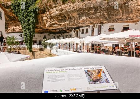 Restaurants und Cafés drängen sich unter einem Felsüberhang entlang der Terrazas Calle Cuevas del Sol in den einzigartigen Pueblos blanco von Setenil de las Bodegas, Spanien. Die Bewohner des kleinen Dorfes Setenil leben seit dem neolithikum in Höhlenhäusern. Stockfoto