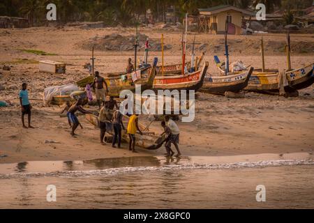 Die Gruppe der Fischer und das Fischerboot (Piroga) am Sandstrand in Accra, Ghana am Ende des Arbeitstages in Westafrika. Stockfoto