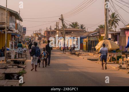 Die afrikanischen Menschen mit Kindern laufen auf den staubigen Straßen von Accra, der Hauptstadt von Ghana (Westafrika) entlang der kleinen lokalen Geschäfte und der schmutzigen Straße Stockfoto