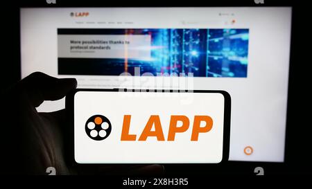 Person, die ein Mobiltelefon mit dem Logo der deutschen Kabelgesellschaft Lapp Holding SE vor der Webseite hält. Schwerpunkt auf dem Display des Telefons. Stockfoto