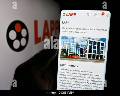 Person, die ein Mobiltelefon hält, mit Webseite der deutschen Kabelgesellschaft Lapp Holding SE vor dem Firmenlogo. Konzentrieren Sie sich auf die Mitte des Telefondisplays. Stockfoto